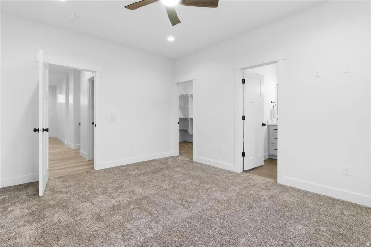 Unfurnished bedroom with a walk in closet, light carpet, ceiling fan, recessed lighting, and connected bathroom