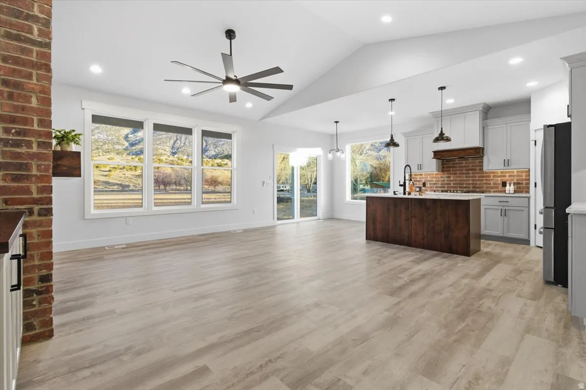 Kitchen with open floor plan, hanging light fixtures, light wood-style flooring, a center island with sink, and freestanding refrigerator