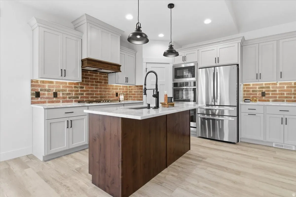Kitchen featuring appliances with stainless steel finishes, light stone counters, pendant lighting, white cabinetry, and light wood-style floors