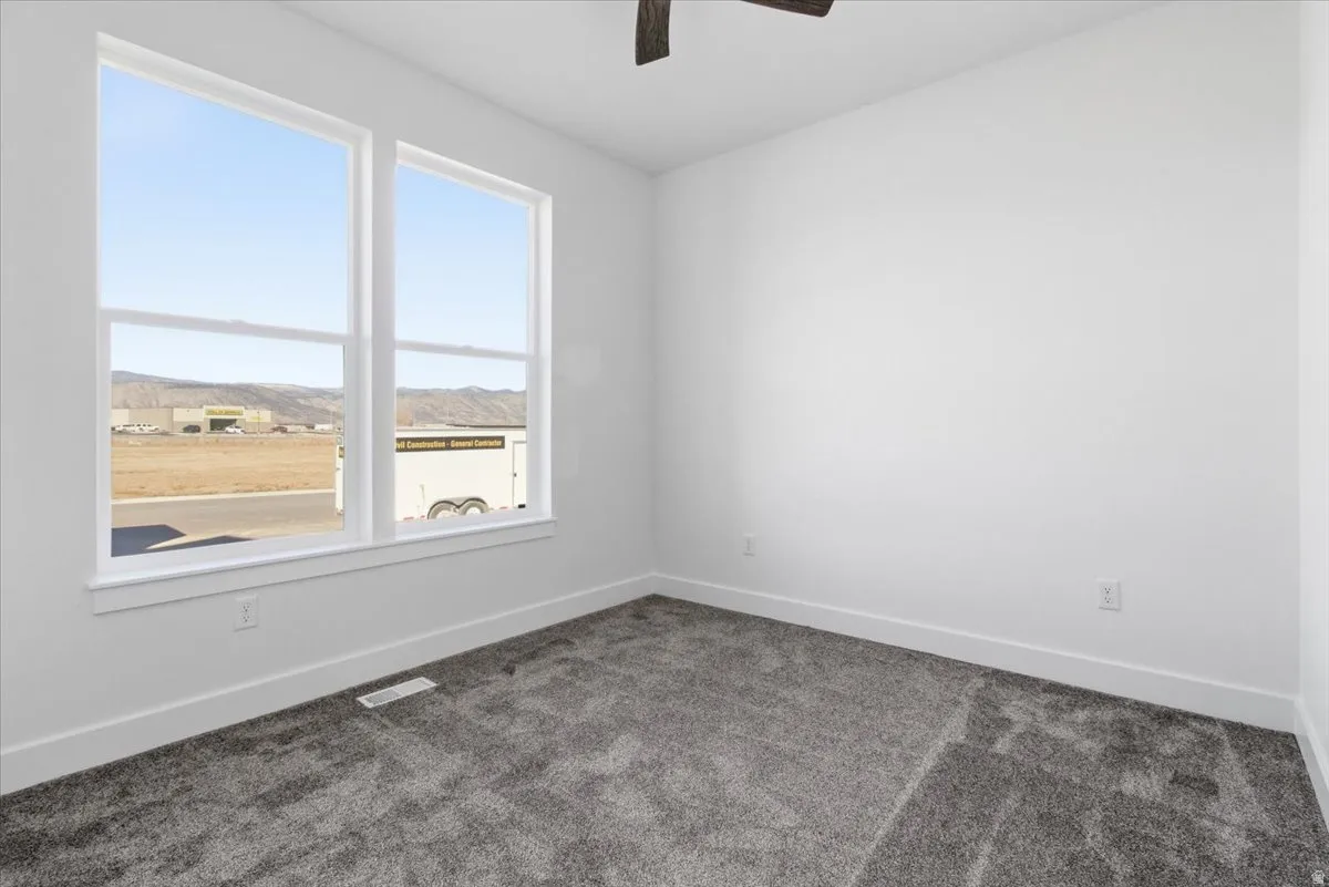 Unfurnished room featuring dark carpet, a mountain view, and ceiling fan