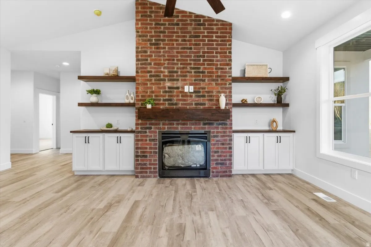 Unfurnished living room featuring a brick fireplace, light wood finished floors, recessed lighting, lofted ceiling, and ceiling fan
