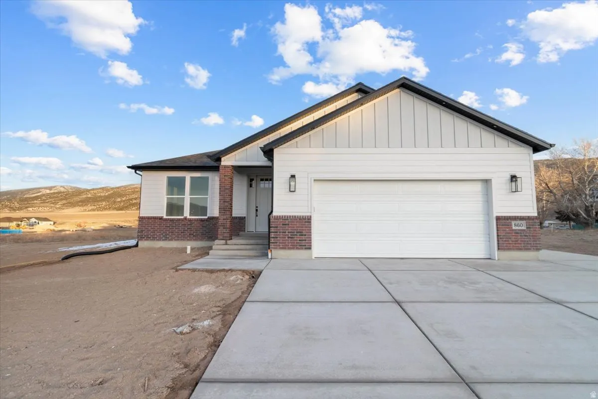 View of front facade featuring brick siding, board and batten siding, driveway, and an attached garage