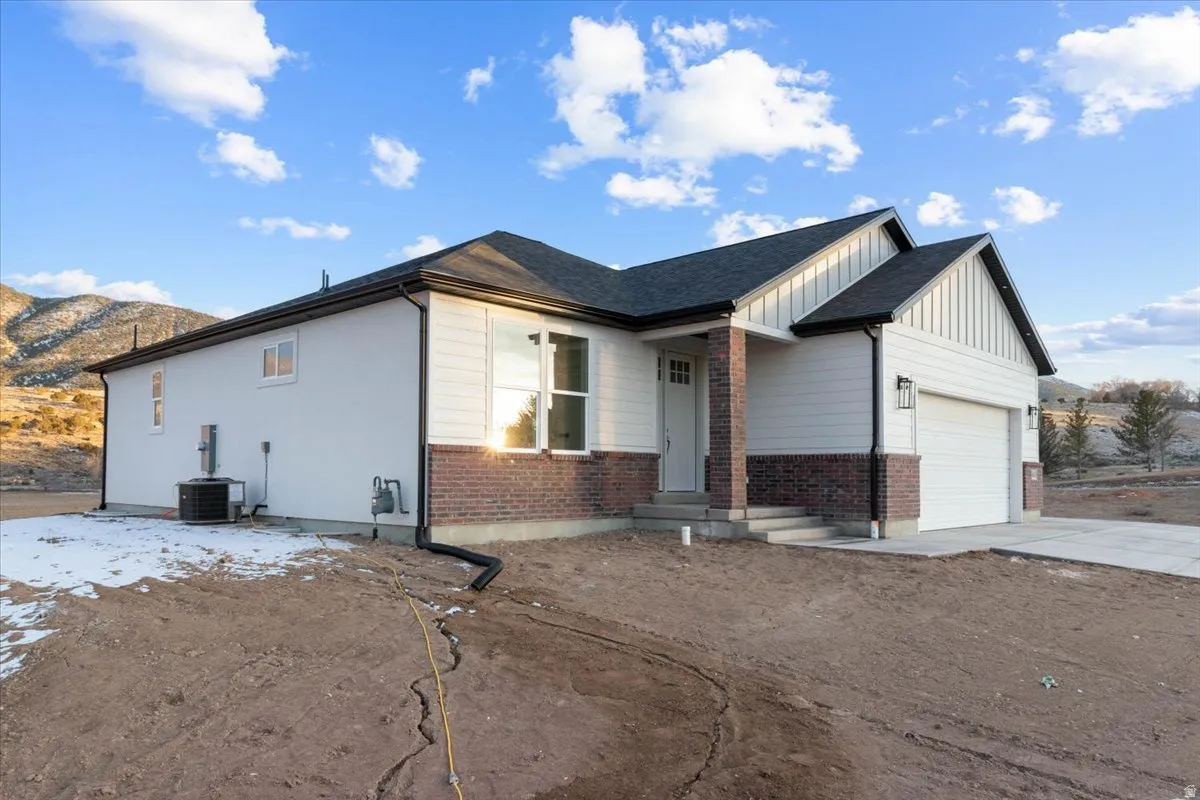 View of front of house with board and batten siding, brick siding, an attached garage, and concrete driveway