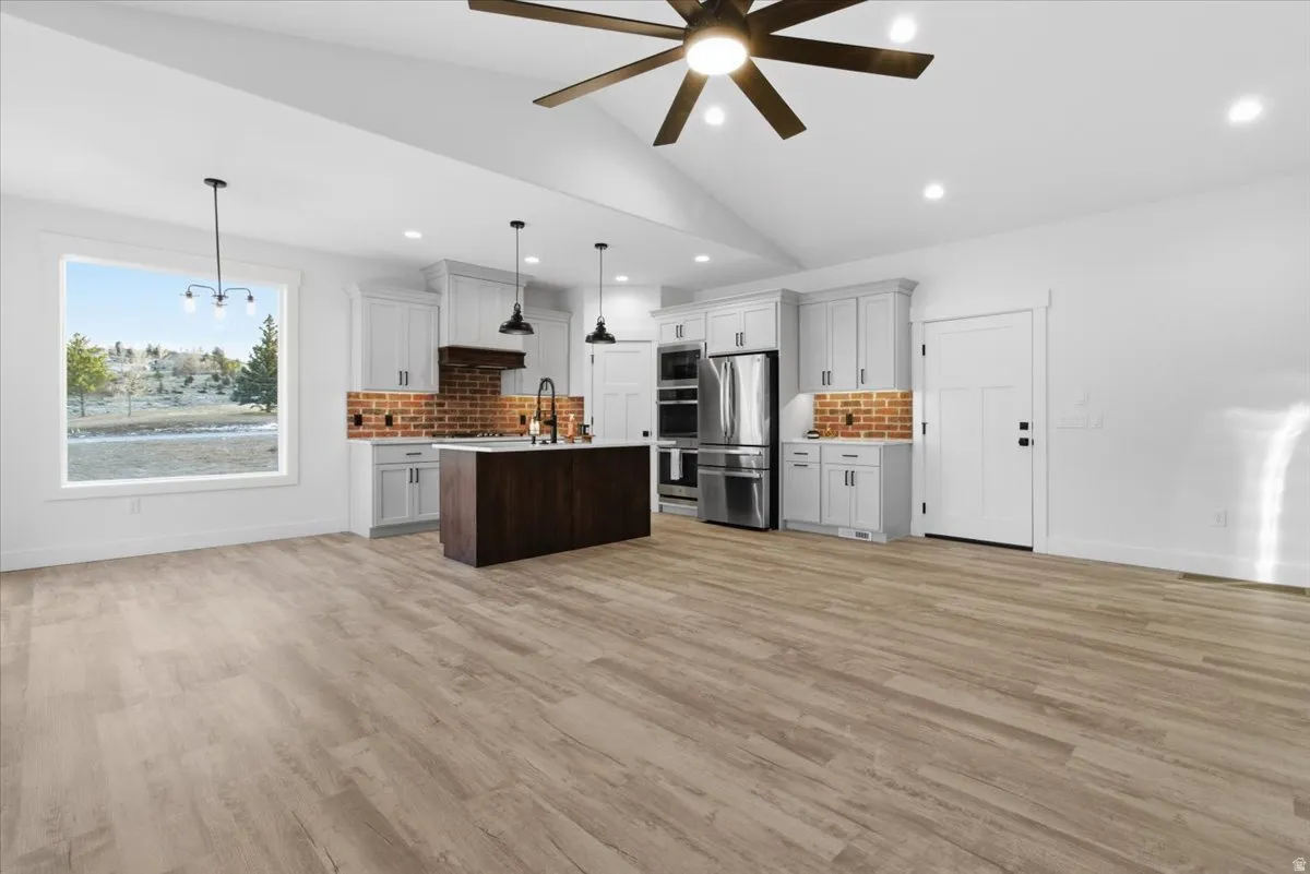 Kitchen featuring open floor plan, lofted ceiling, pendant lighting, white cabinets, and appliances with stainless steel finishes