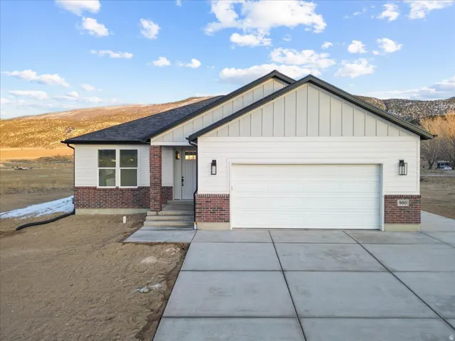 View of front of home featuring board and batten siding, brick siding, an attached garage, and driveway