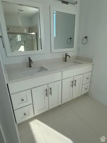 Full bath featuring light tile patterned floors, a marble finish shower, and double vanity
