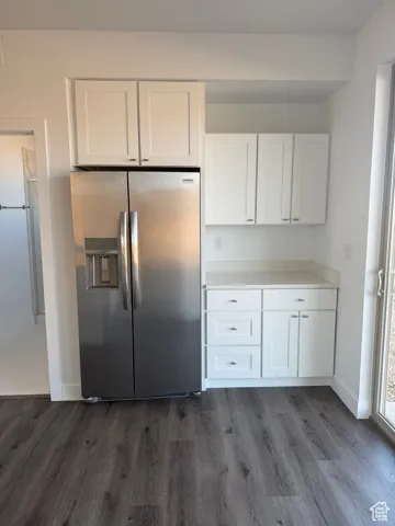 Kitchen featuring white cabinets, stainless steel fridge, light countertops, and dark wood-style floors