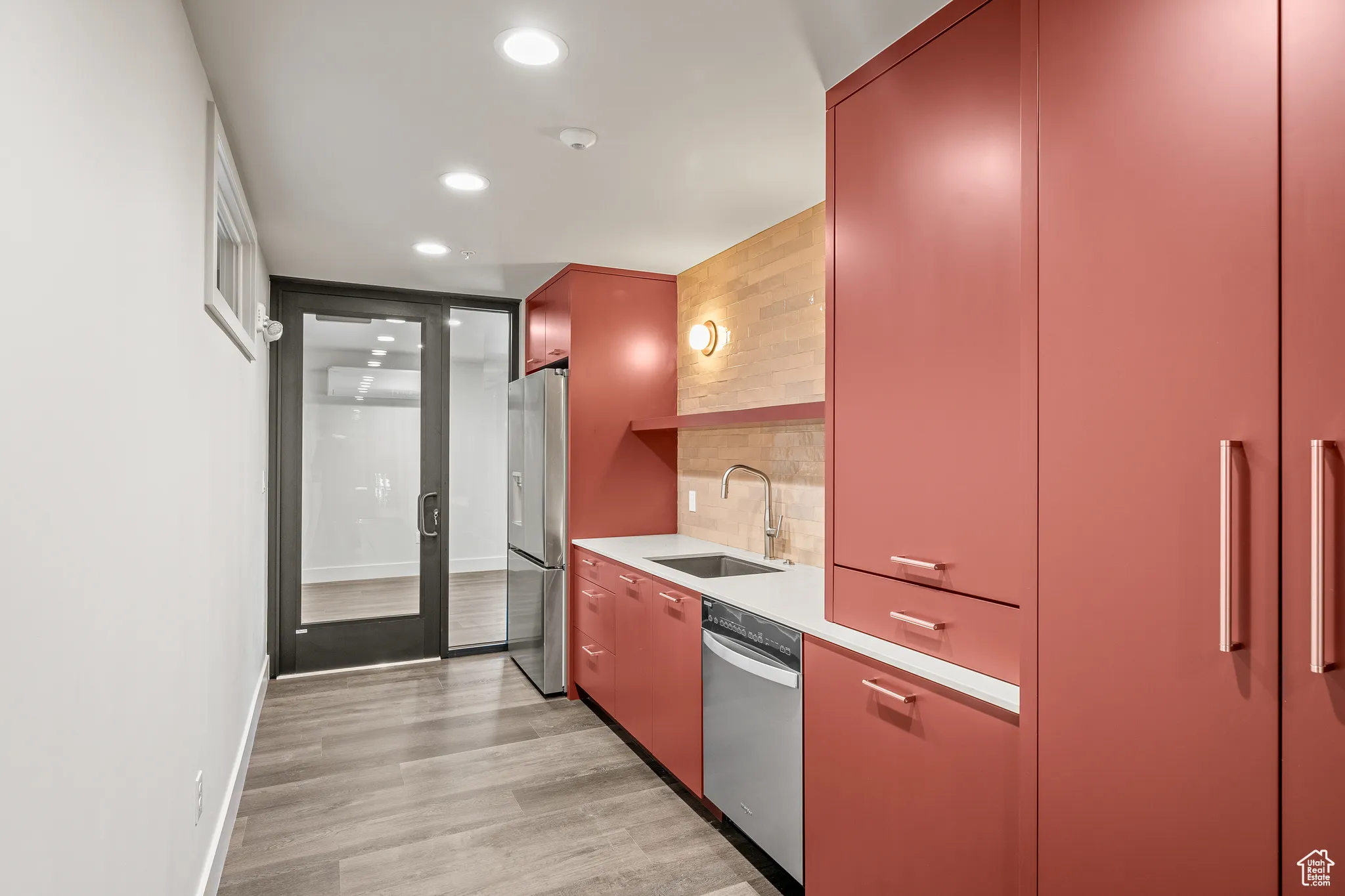 Kitchen featuring modern cabinets, tasteful backsplash, red cabinetry, light wood-type flooring, and stainless steel appliances