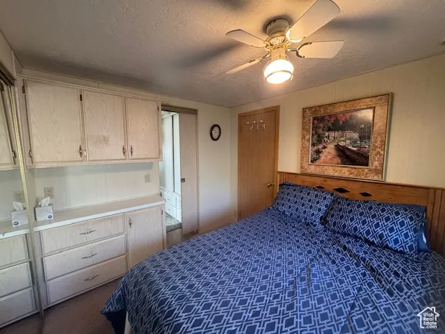 Bedroom featuring wooden walls, a textured ceiling, dark colored carpet, and ceiling fan