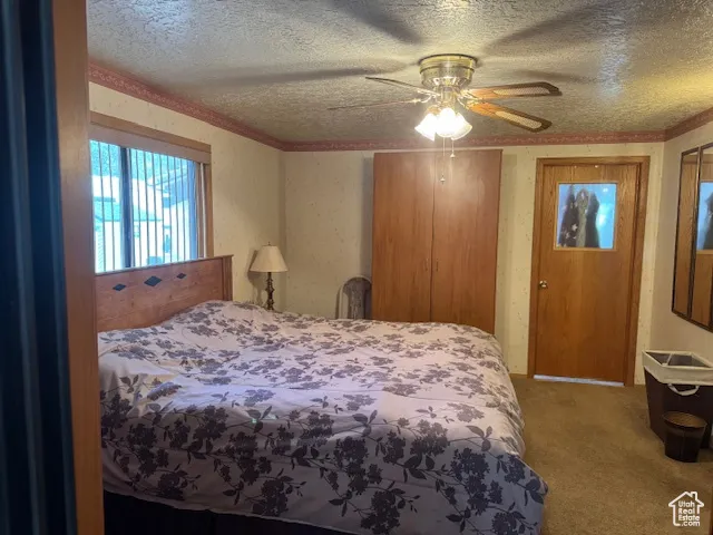 Bedroom with a textured ceiling, carpet flooring, ceiling fan, crown molding, and wallpapered walls