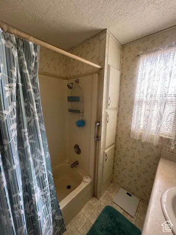 Bathroom with wallpapered walls, a textured ceiling, shower / bath combo, vanity, and light tile patterned floors