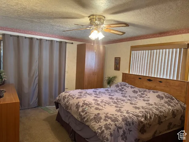 Bedroom featuring a textured ceiling, carpet flooring, wallpapered walls, and a ceiling fan