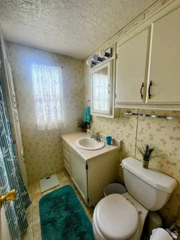 Bathroom featuring vanity, wallpapered walls, a textured ceiling, and light tile patterned floors
