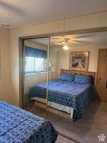 Bedroom featuring wood walls, carpet, a textured ceiling, a ceiling fan, and a closet