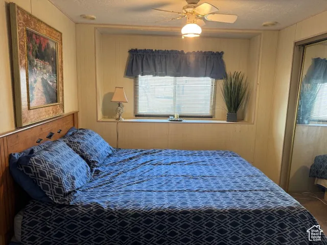 Bedroom featuring a textured ceiling, a ceiling fan, and wooden walls