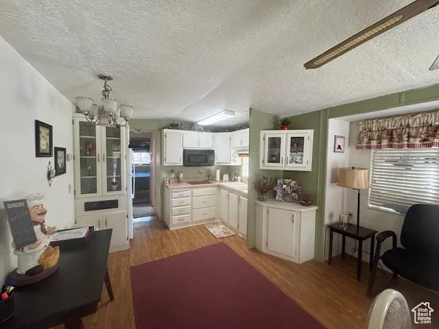 Kitchen featuring white cabinets, light wood-style floors, a chandelier, light countertops, and black appliances