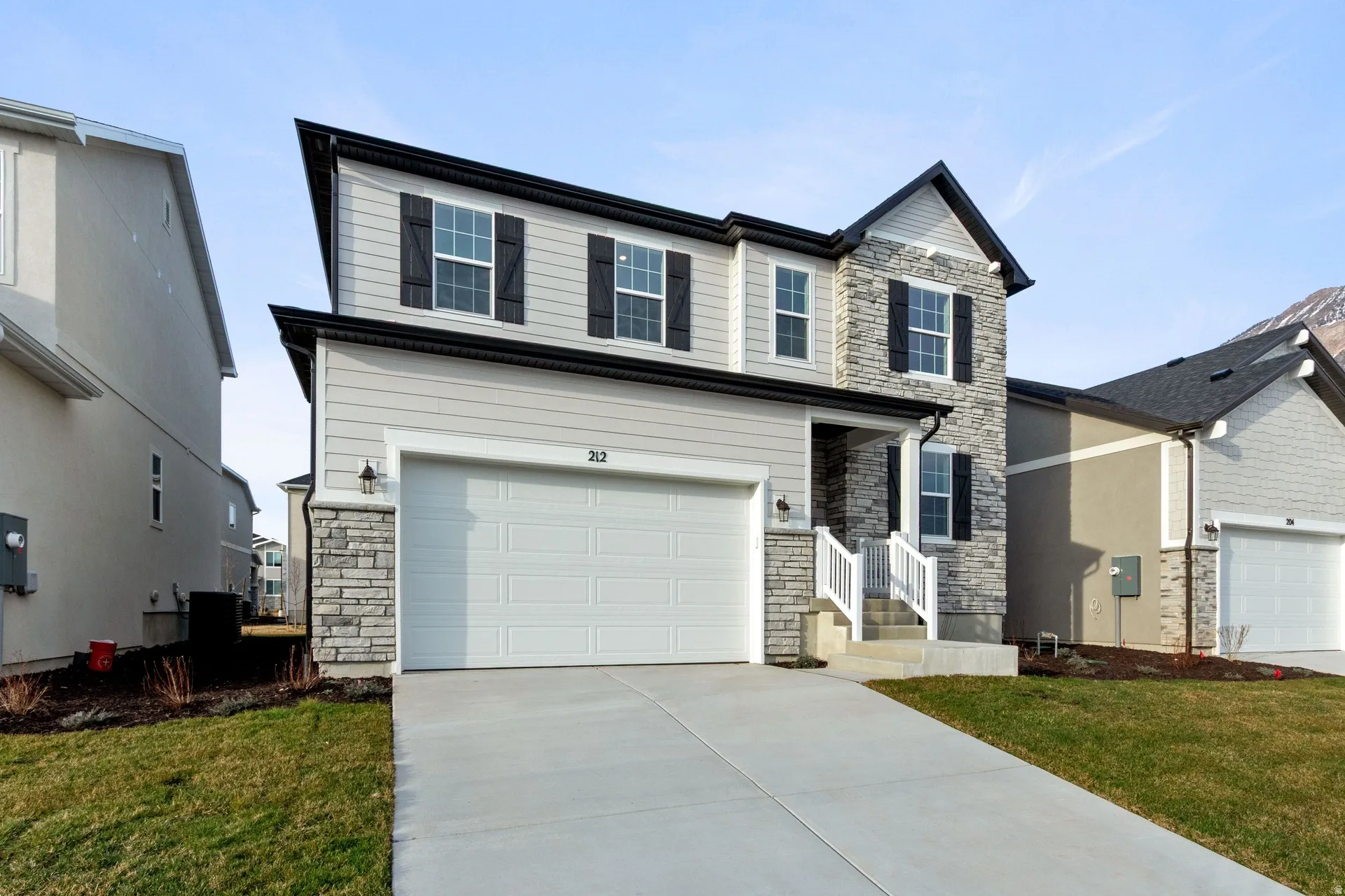 View of front of property with stone siding, concrete driveway, a front lawn, and an attached garage