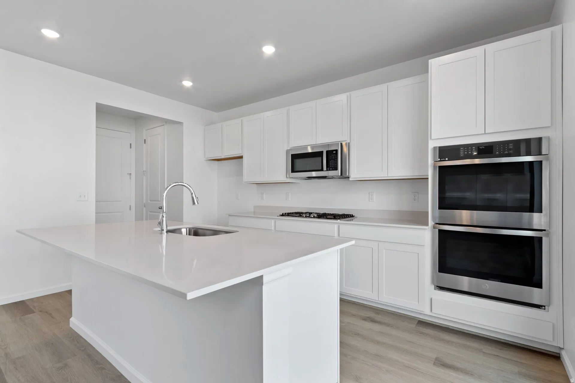Kitchen with stainless steel appliances, white cabinets, a center island with sink, light wood-style floors, and recessed lighting