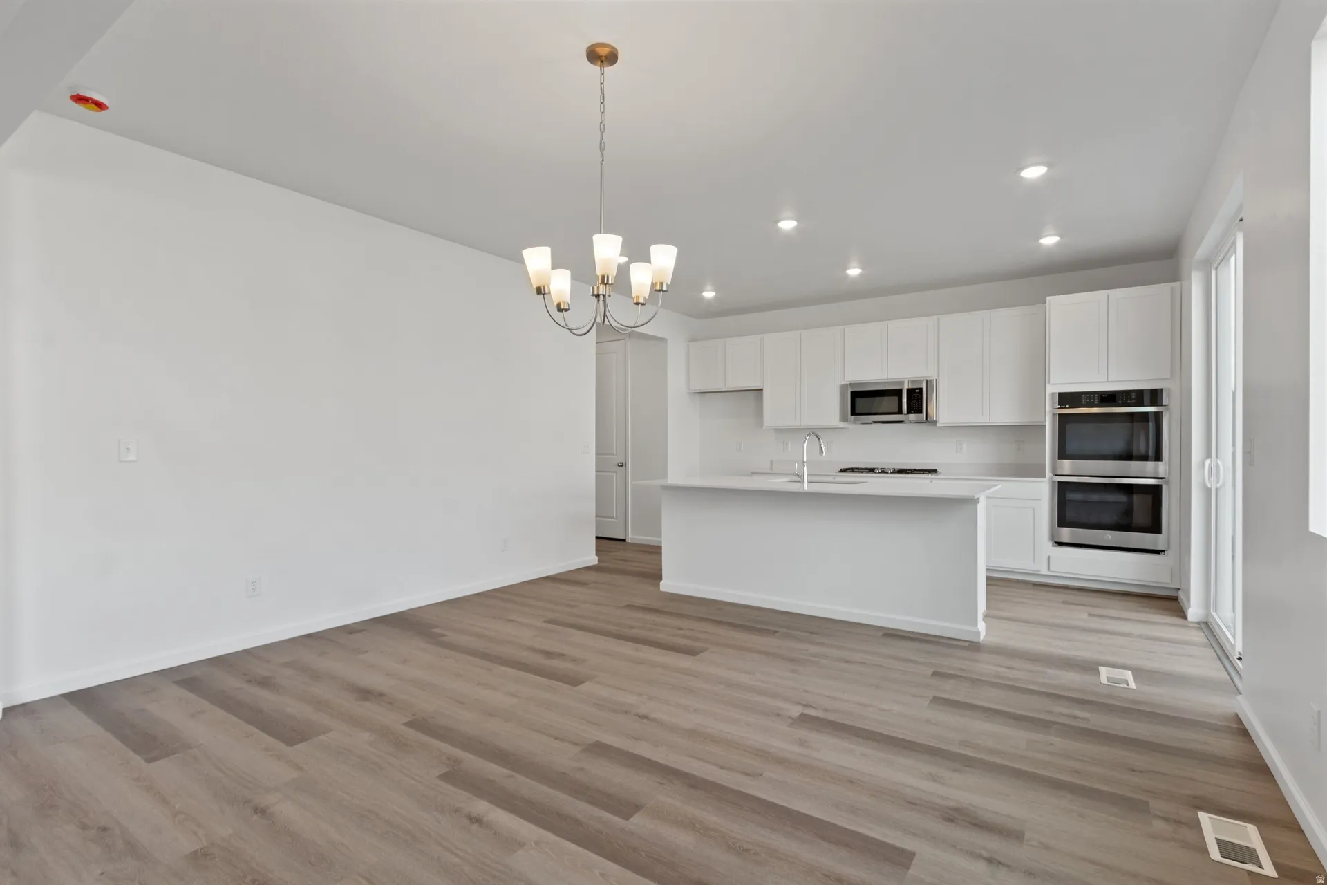 Kitchen featuring white cabinetry, a chandelier, stainless steel appliances, a center island with sink, and open floor plan