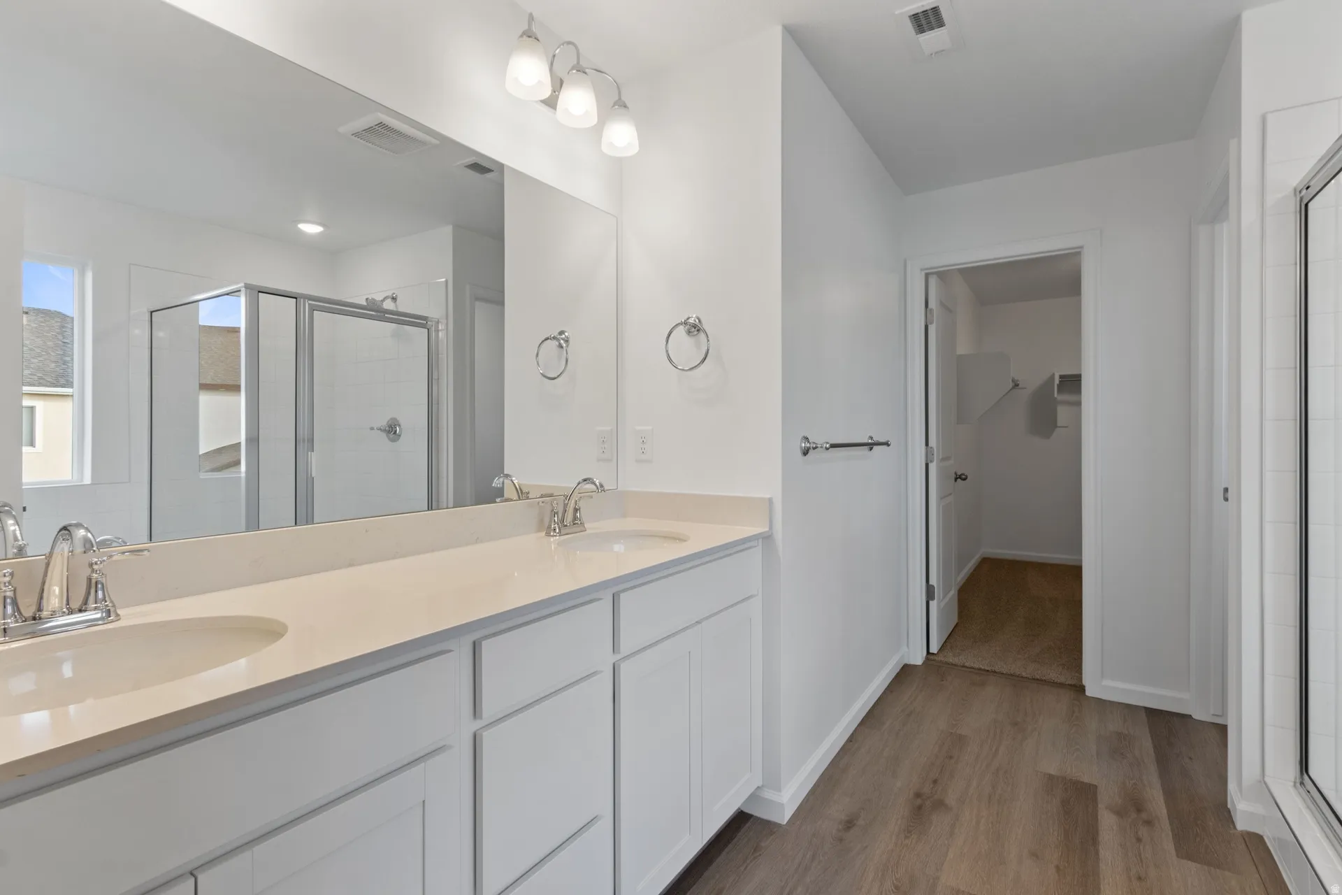 Primary bath featuring a shower stall, double vanity, light wood-type flooring, and a walk in closet