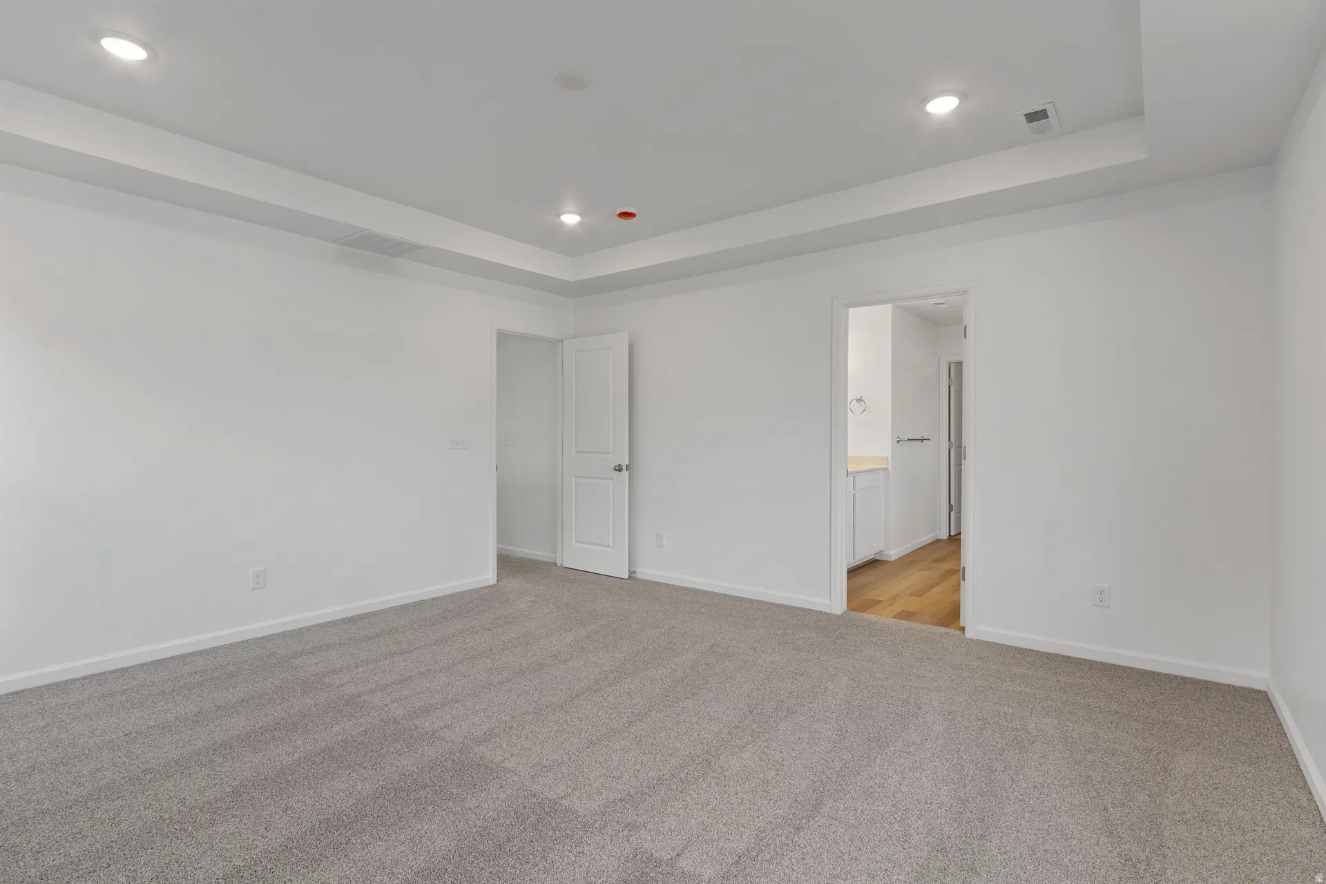 Primary bedroom with light carpet, a tray ceiling, recessed lighting, and ensuite bath