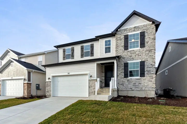 View of front of house with stone siding, a garage, driveway, and a front yard