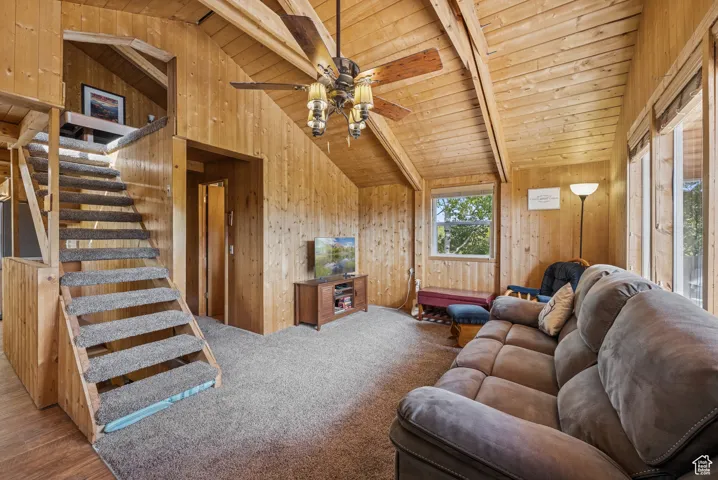 Living area featuring wooden walls, wood ceiling, stairs, ceiling fan, and carpet flooring