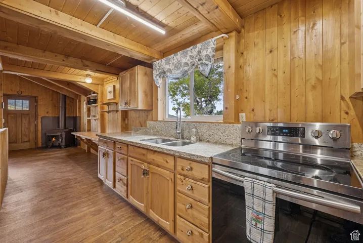 Kitchen with stainless steel electric range oven, wood walls, light stone countertops, a wood stove, and dark wood-style floors