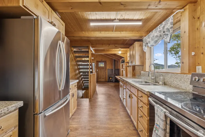 Kitchen featuring stainless steel appliances, light stone counters, wood walls, light wood-type flooring, and a wooden ceiling with exposed beams