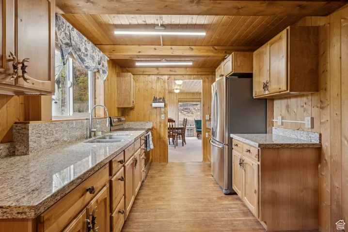 Kitchen with wood walls, freestanding refrigerator, white stove, light wood-style floors, and a wood ceiling with exposed beams