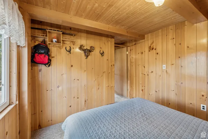 Bedroom featuring wood walls, carpet flooring, a wooden ceiling with exposed beams, a closet, and multiple windows