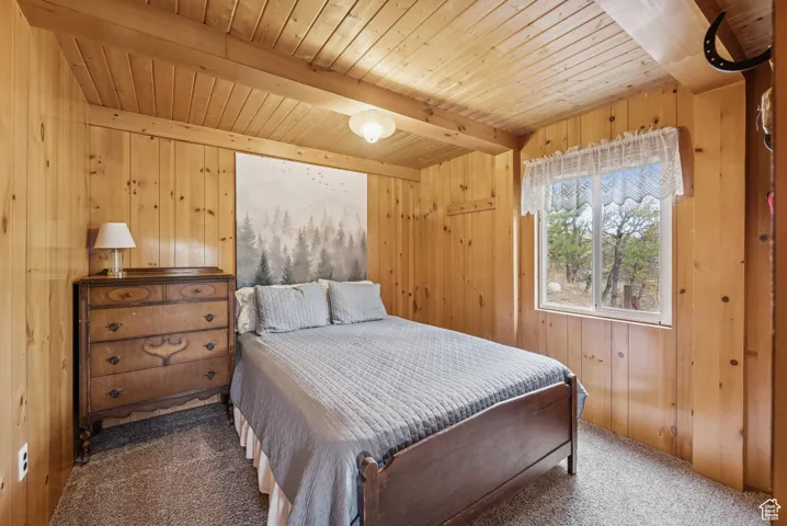 Carpeted bedroom with wood walls and a wood ceiling with exposed beams