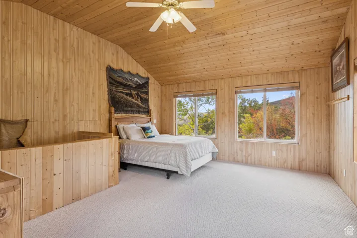 Bedroom with wooden walls, vaulted ceiling, carpet floors, wooden ceiling, and a ceiling fan