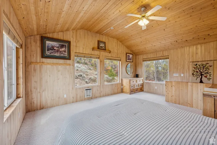 Unfurnished bedroom with vaulted ceiling, carpet flooring, wooden walls, and wooden ceiling