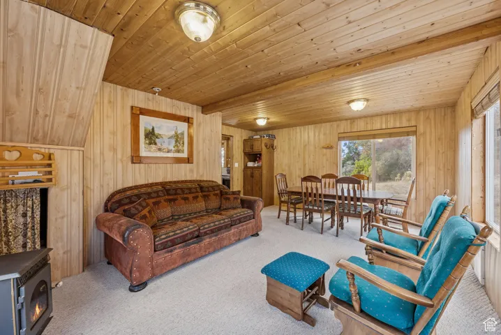 Carpeted living area with wooden walls, a wood ceiling with exposed beams, and a wood stove