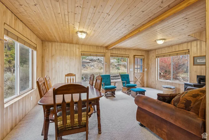 Dining space with wooden walls, carpet flooring, and a wood ceiling with exposed beams