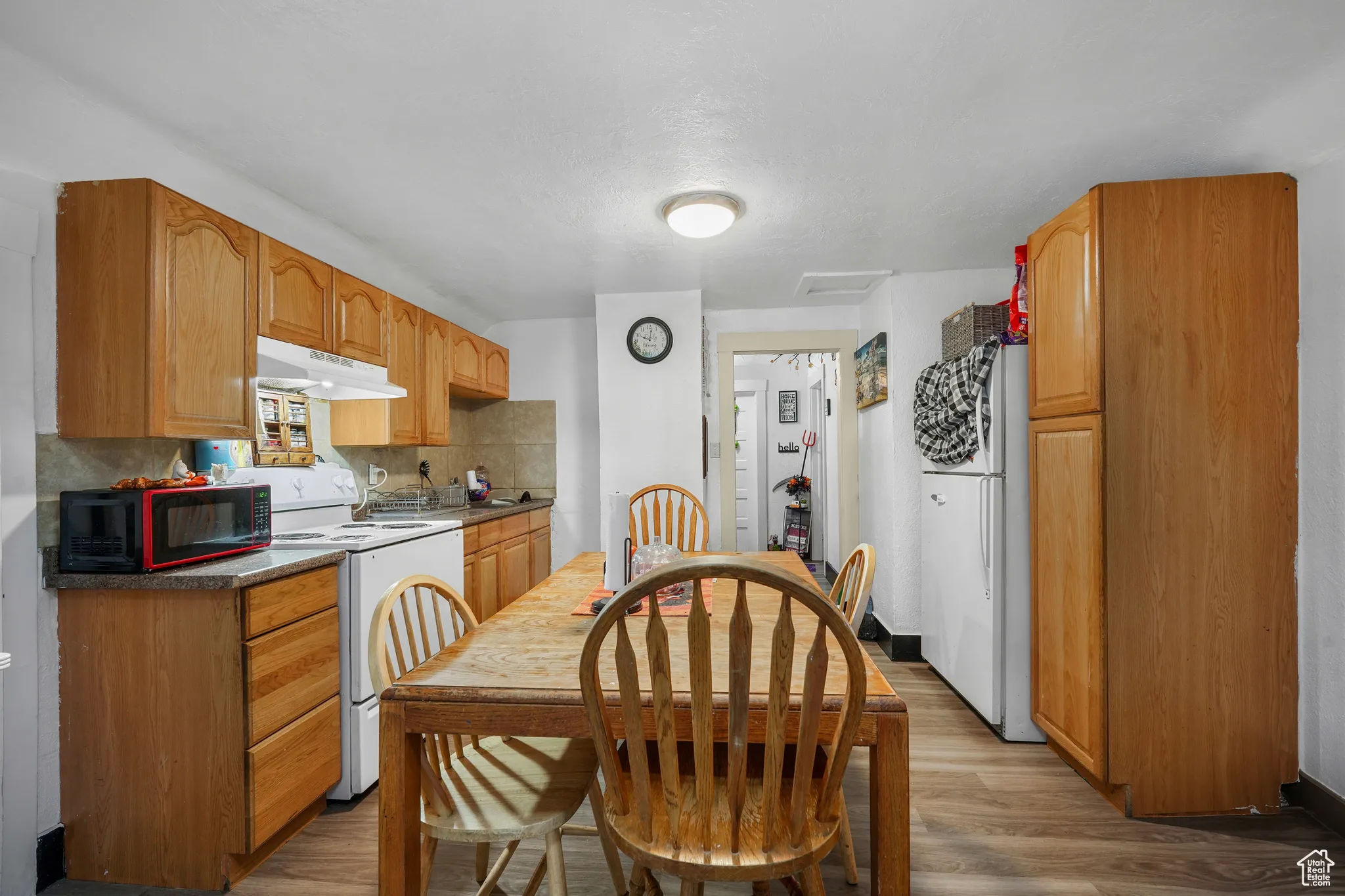 Kitchen featuring wood finished floors, white appliances, tasteful backsplash, under cabinet range hood, and dark countertops