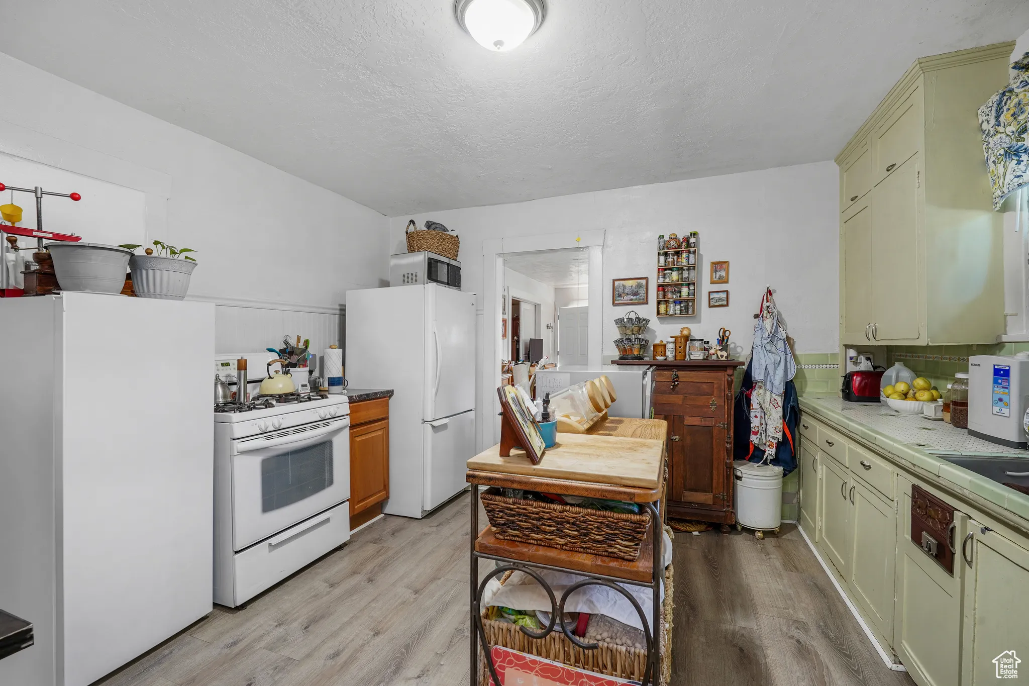 Kitchen featuring white appliances, light wood-style floors, a textured ceiling, and backsplash