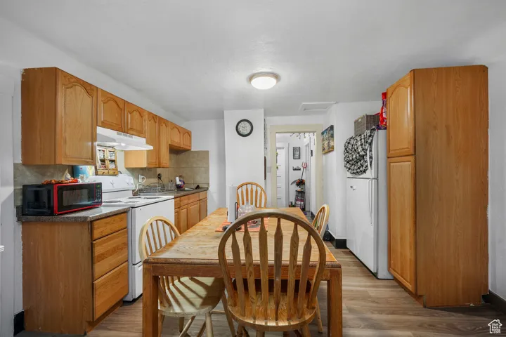 Kitchen featuring wood finished floors, white appliances, tasteful backsplash, under cabinet range hood, and dark countertops