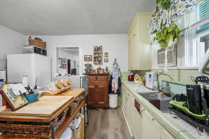 Kitchen with light wood-style floors, freestanding refrigerator, stainless steel microwave, decorative backsplash, and a textured ceiling