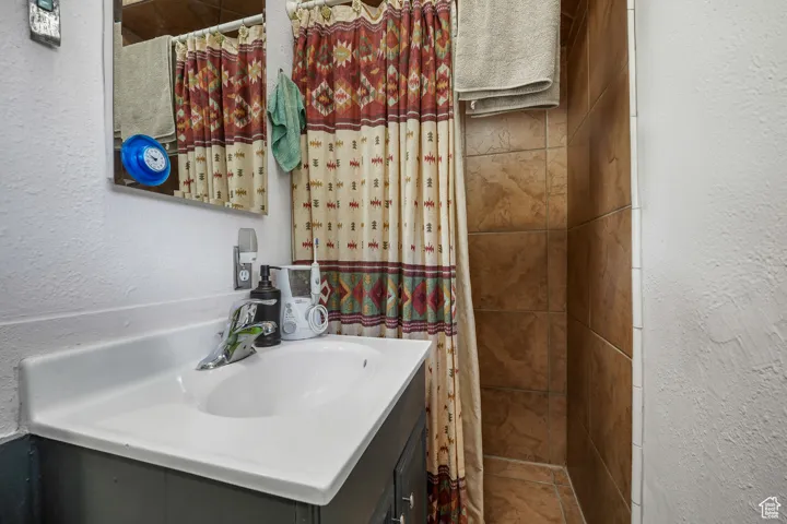 Full bath featuring a textured wall, vanity, and curtained shower