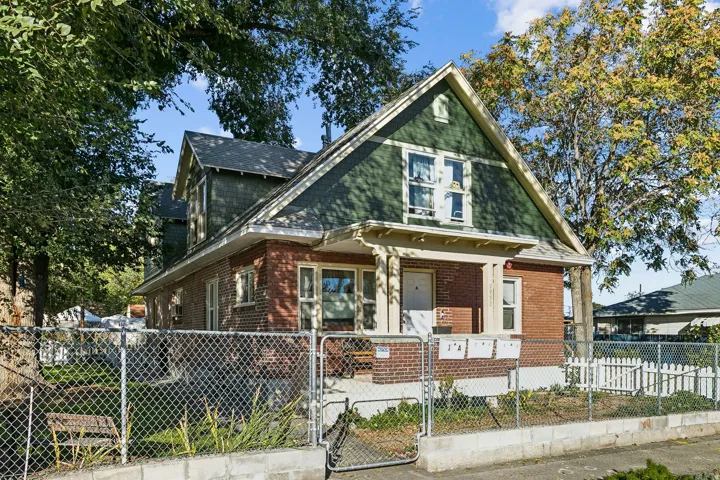 View of front of home featuring a gate, brick siding, a fenced front yard, covered porch, and roof with shingles