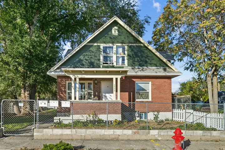 View of front of property featuring covered porch, a gate, brick siding, a fenced front yard, and roof with shingles