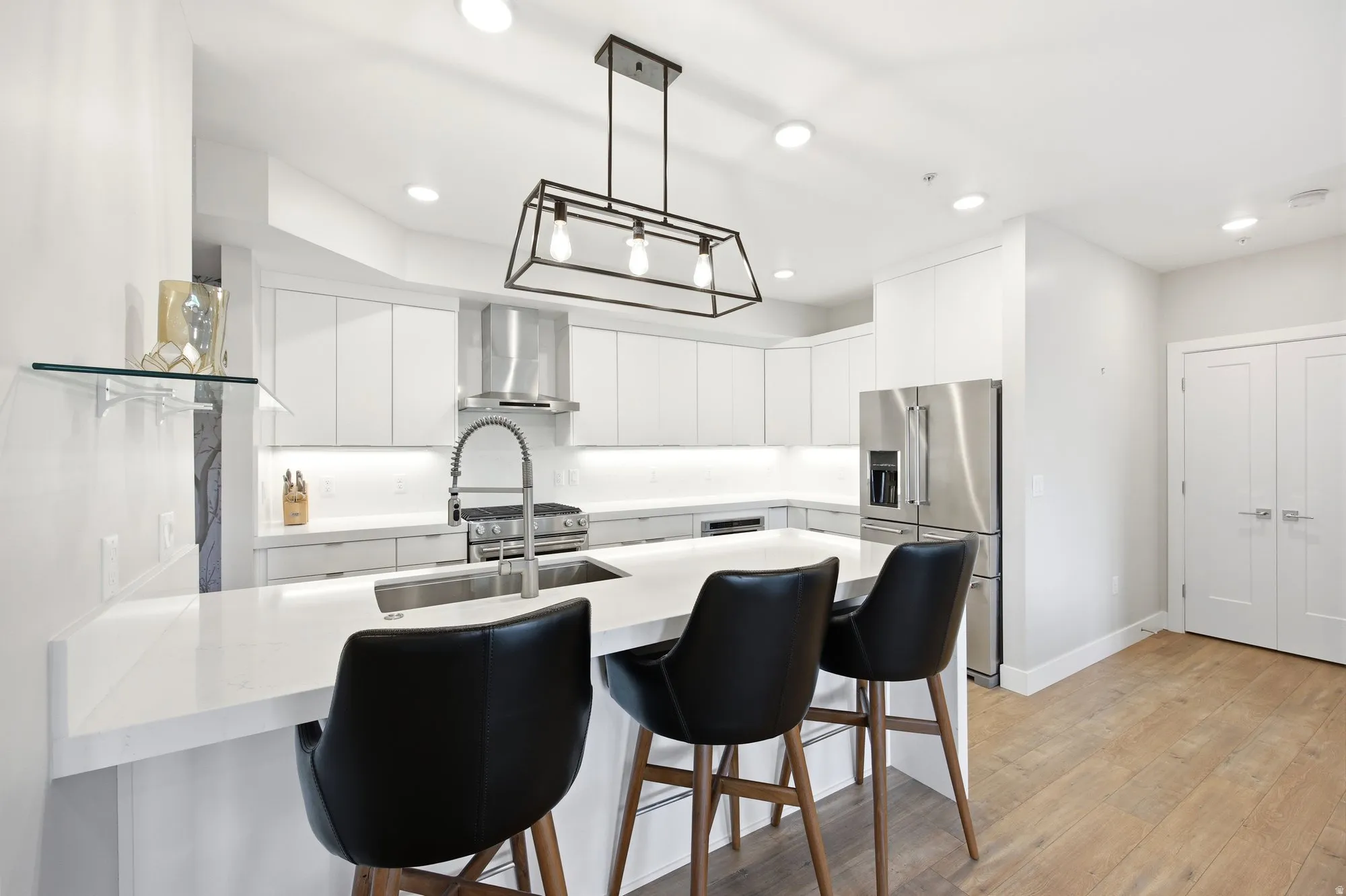 Kitchen featuring a breakfast bar, white cabinets, a peninsula, high end refrigerator, and light wood-style floors