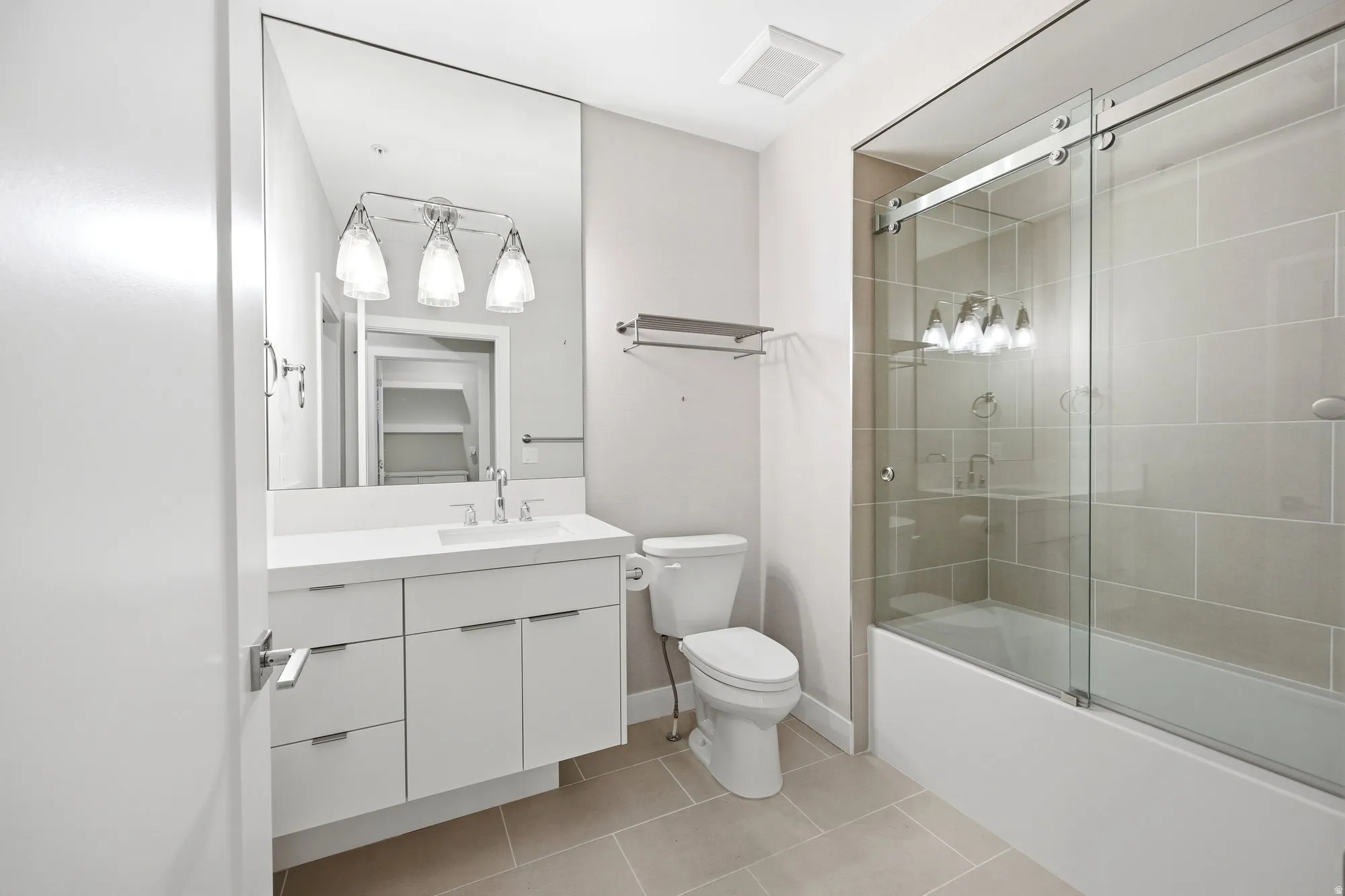 Bathroom featuring vanity, light tile patterned floors, and shower / bath combination with glass door
