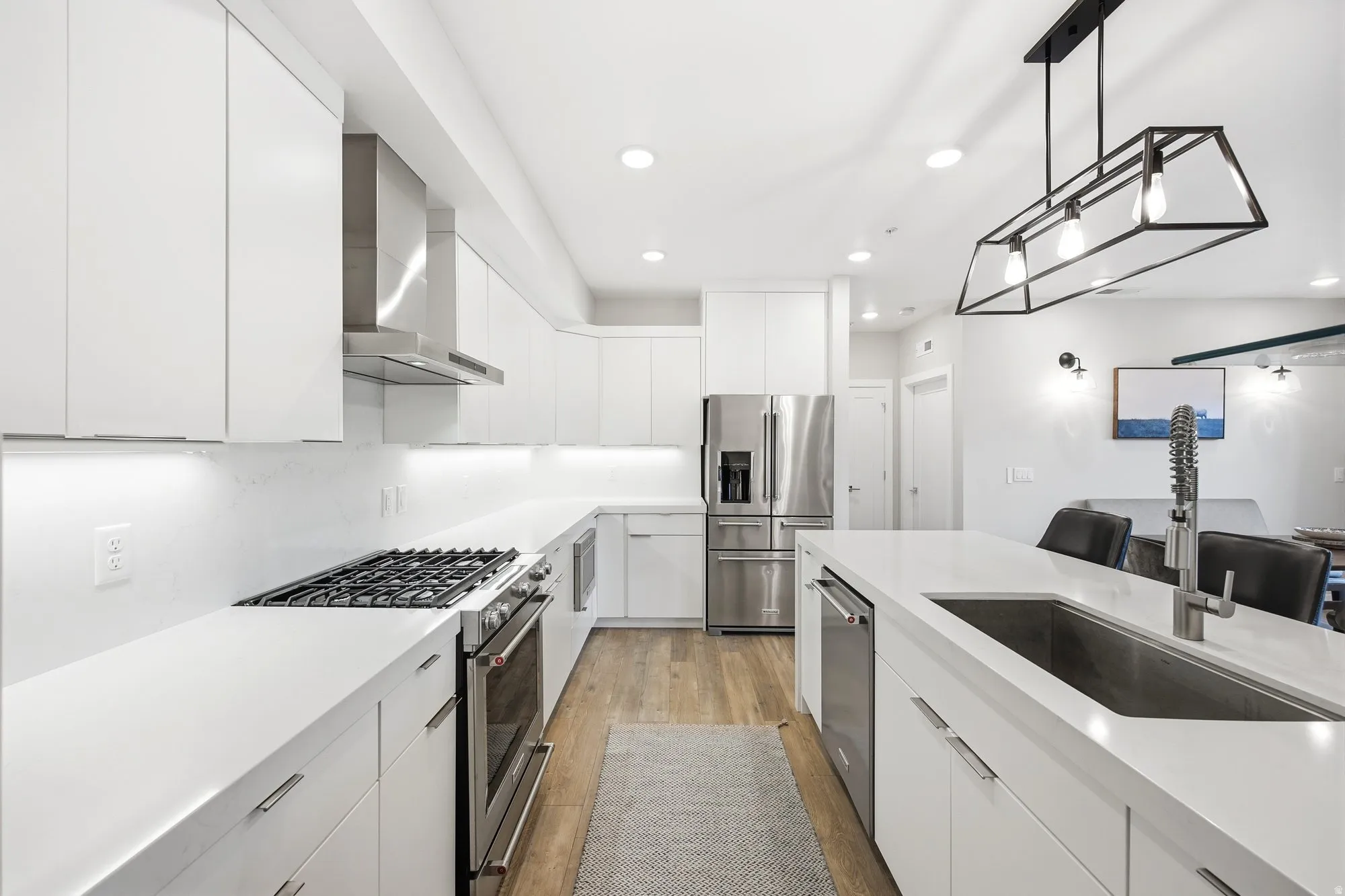 Kitchen featuring stainless steel appliances, white cabinetry, pendant lighting, modern cabinets, and light wood-style flooring