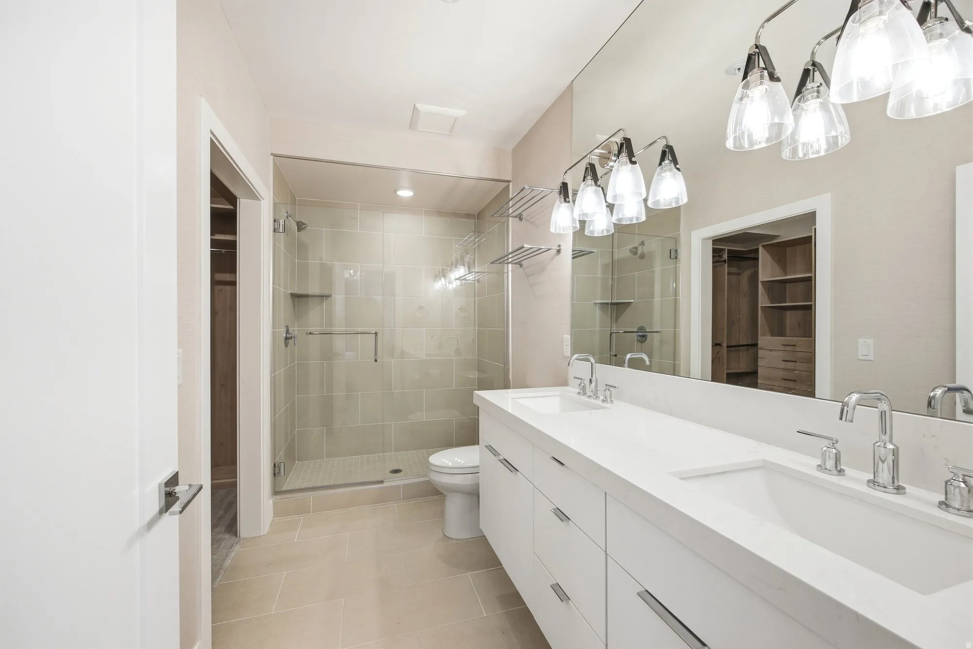 Primary Bathroom featuring a walk in closet, double vanity, a stall shower, and light tile patterned floors