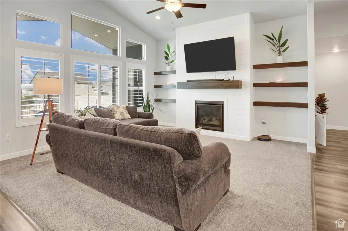 Living room with a large fireplace, a ceiling fan, high vaulted ceiling, light wood-type flooring, and recessed lighting