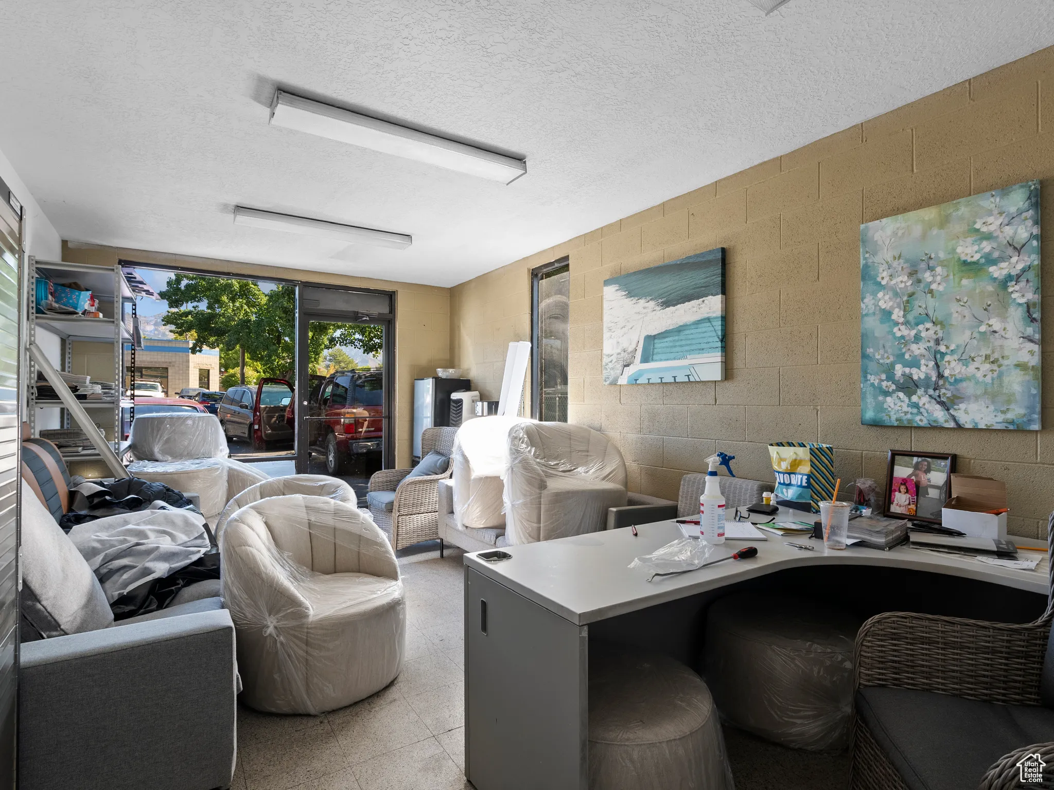 Living room with concrete block wall, a textured ceiling, a desk, and light flooring