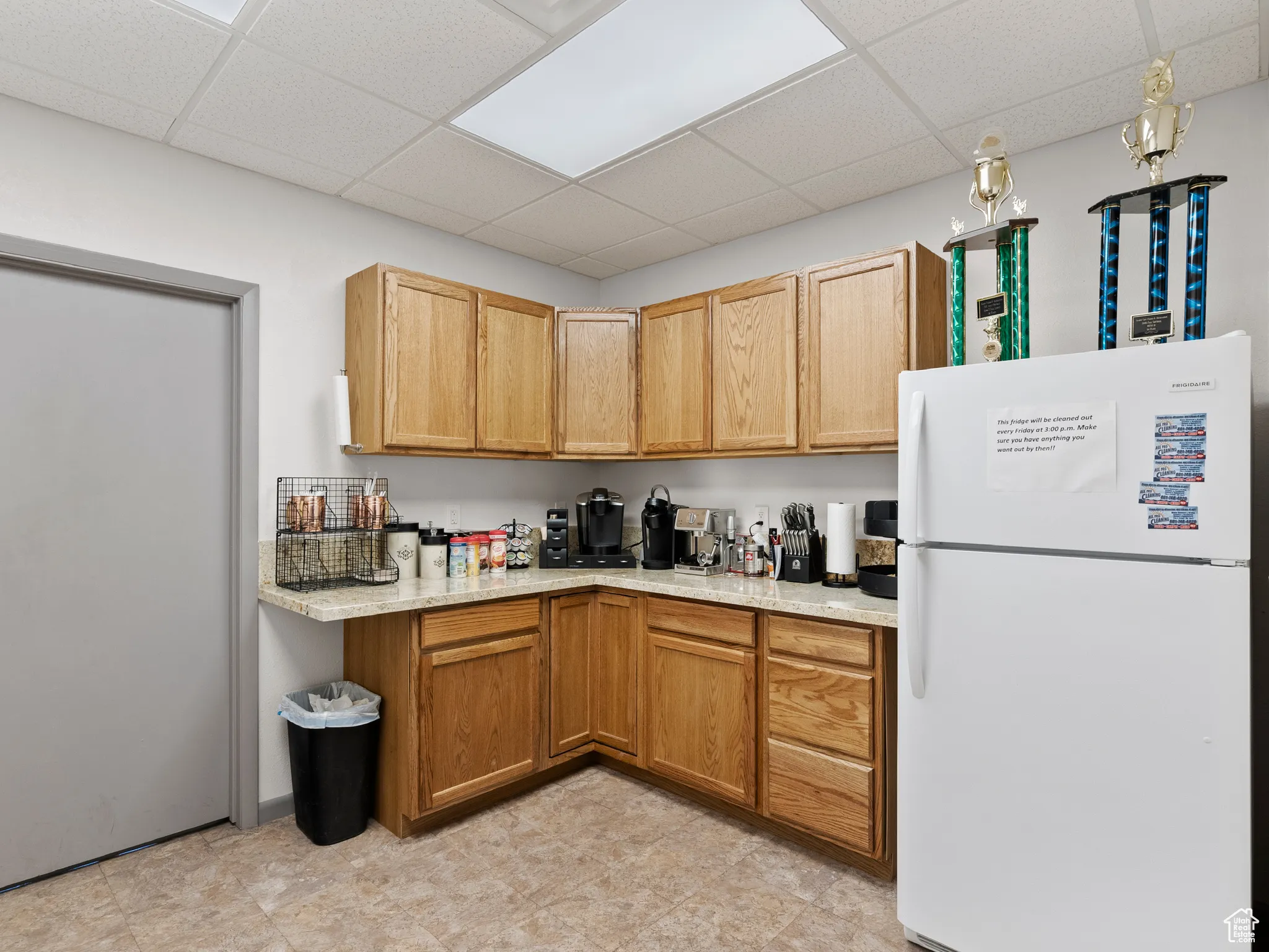 Kitchen with freestanding refrigerator, a drop ceiling, and light stone counters